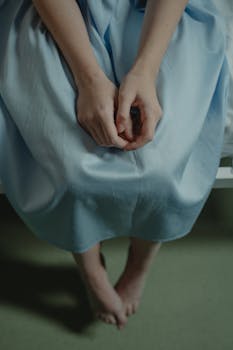 A patient sitting with hands together, wearing a hospital gown, close-up view.