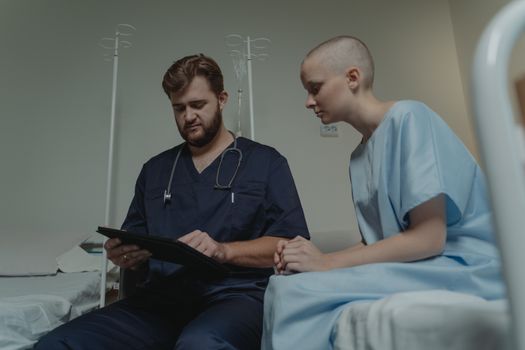Doctor consulting with a young patient in a hospital room using a digital tablet.