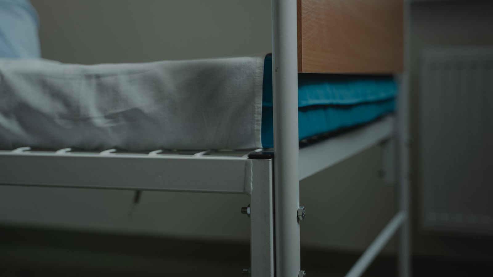 Close-up view of a hospital bed with white linens and metal frame, indoors.
