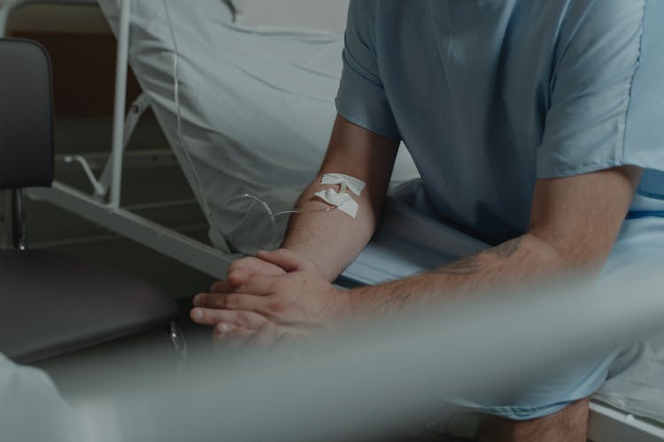 Man Wearing A Hospital Gown Sitting On The Bed