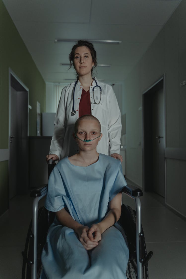 A Doctor Pushing The Wheelchair With Hairless Patient