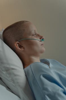 Bald woman in hospital bed with nasal cannula, showing resilience and hope.