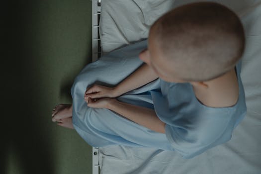 Bald patient sitting on hospital bed, expressing vulnerability and introspection.