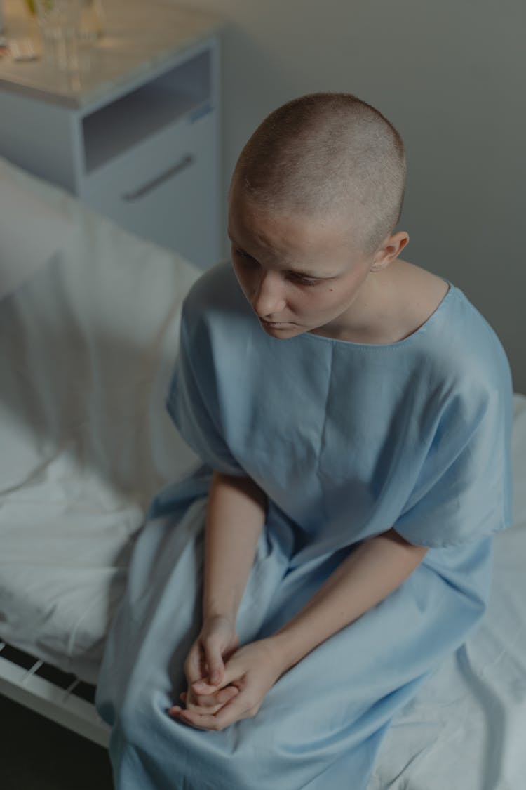 Emotional Woman Wearing A Hospital Gown Sitting On The Bed