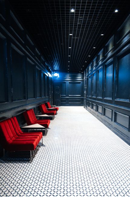 Modern interior of corridor with red sofas and small tables under shiny lamps on ceiling