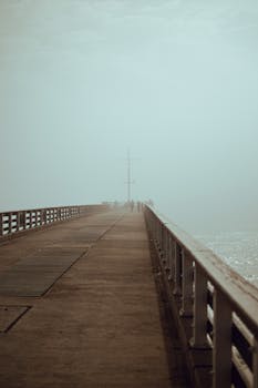 A serene view of an empty pier enveloped in mist, extending into the distance.