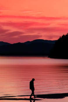Peaceful lakeside scene with a silhouette against a vibrant sunset sky.