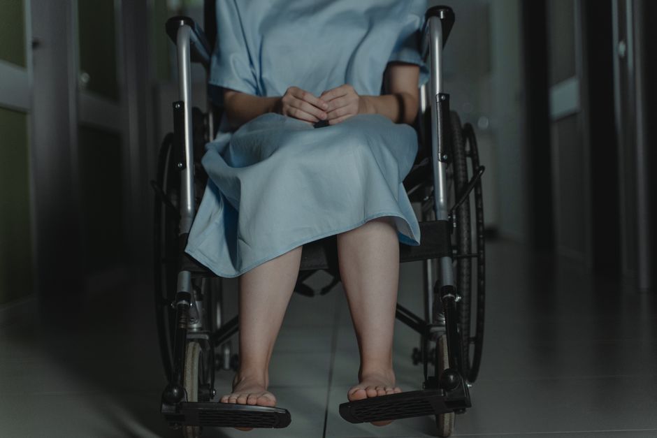 薄暗い廊下で病院のガウンを着たまま、車椅子に座っている裸足の人。