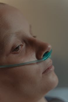 Close-up of a woman lying in a hospital bed with nasal cannula oxygen support.