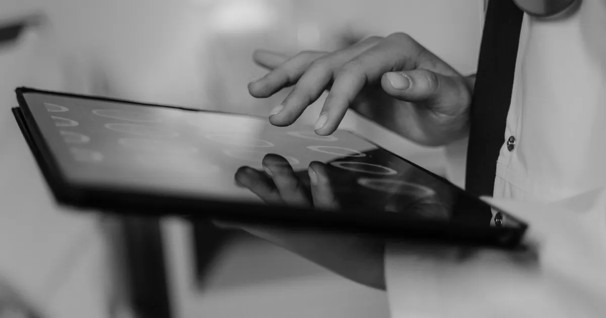 A hand touching a tablet screen, in black and white, representing AI medical malpractice liability 2026