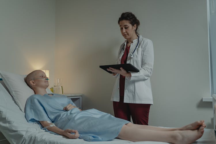 Doctor Looking At A Digital Tablet While Standing Beside A Patient