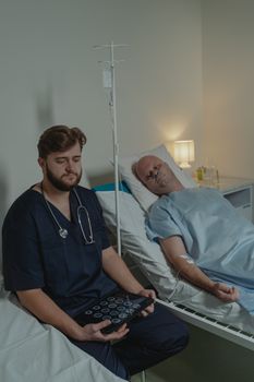 Doctor attends to patient in hospital bed with medical equipment and tablet.