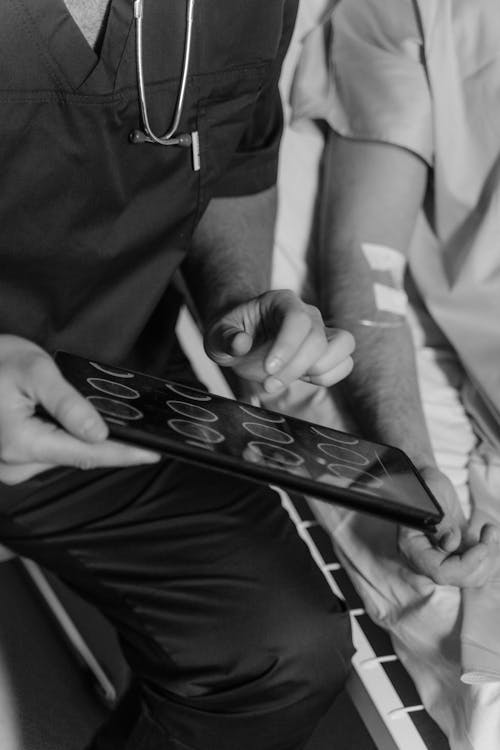 Grayscale Photo of a Doctor Holding a Digital Tablet