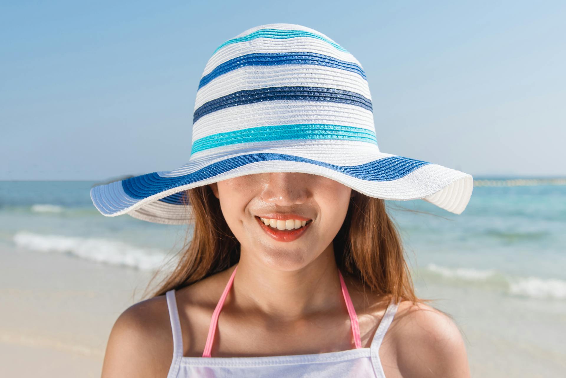 Young woman in a sun hat smiling on a sunny beach day by the sea.