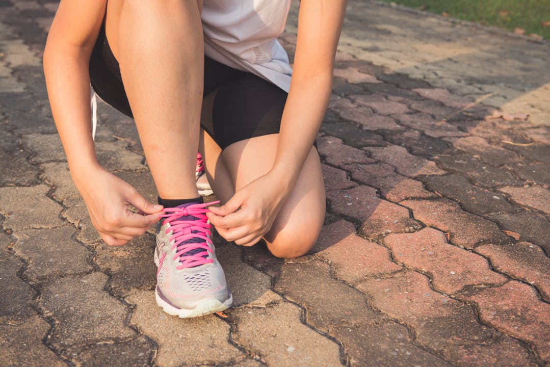 Free Adult woman tying pink laces on running shoes outdoors. Focuses on fitness and lifestyle.