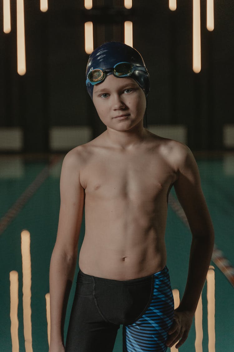 A Shirtless Boy Wearing A Swimming Cap And Goggles On His Head