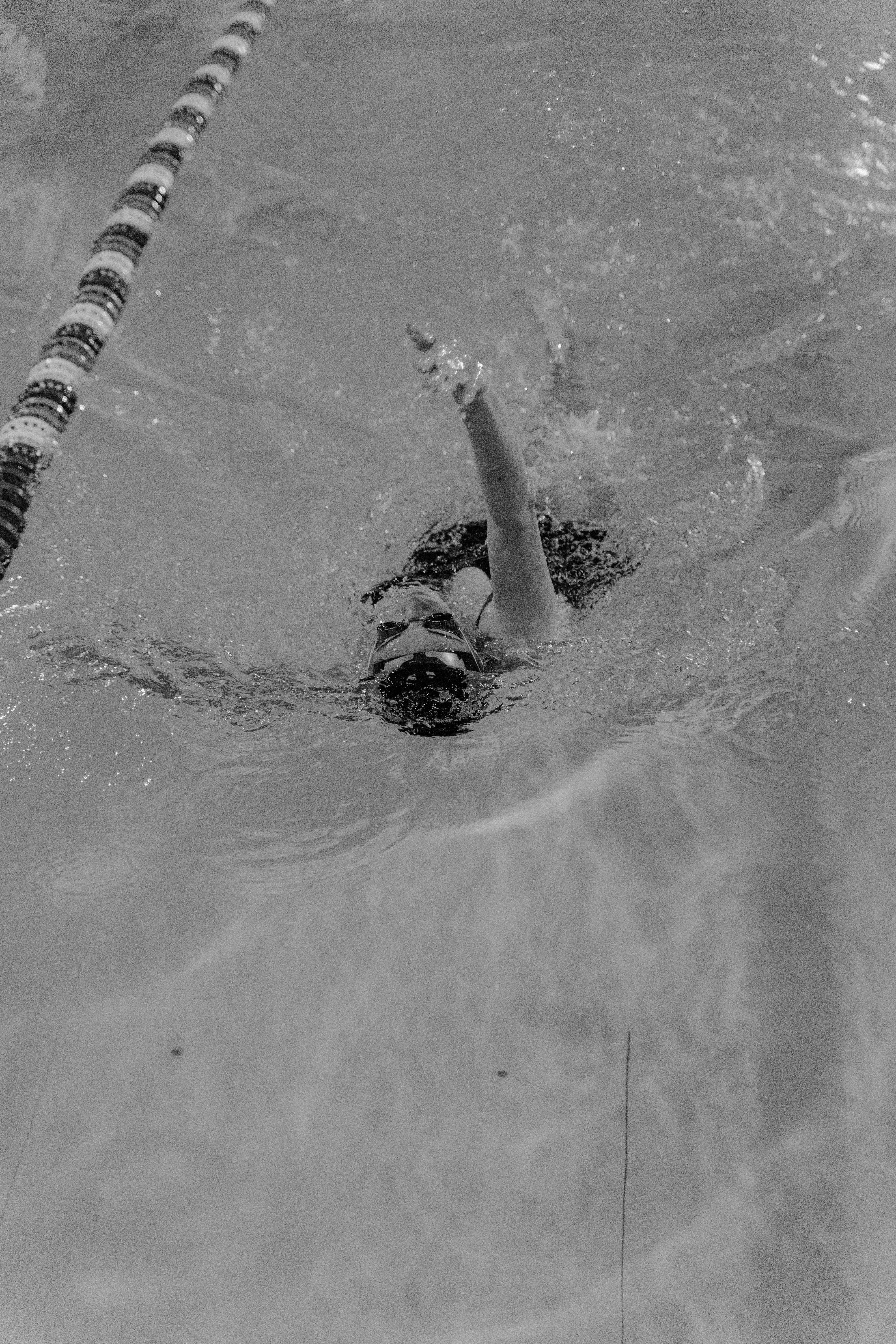 An athlete performing backstroke in a pool, captured in black and white.