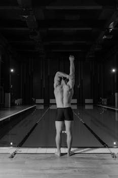 Male swimmer stretching at indoor pool, black and white view.