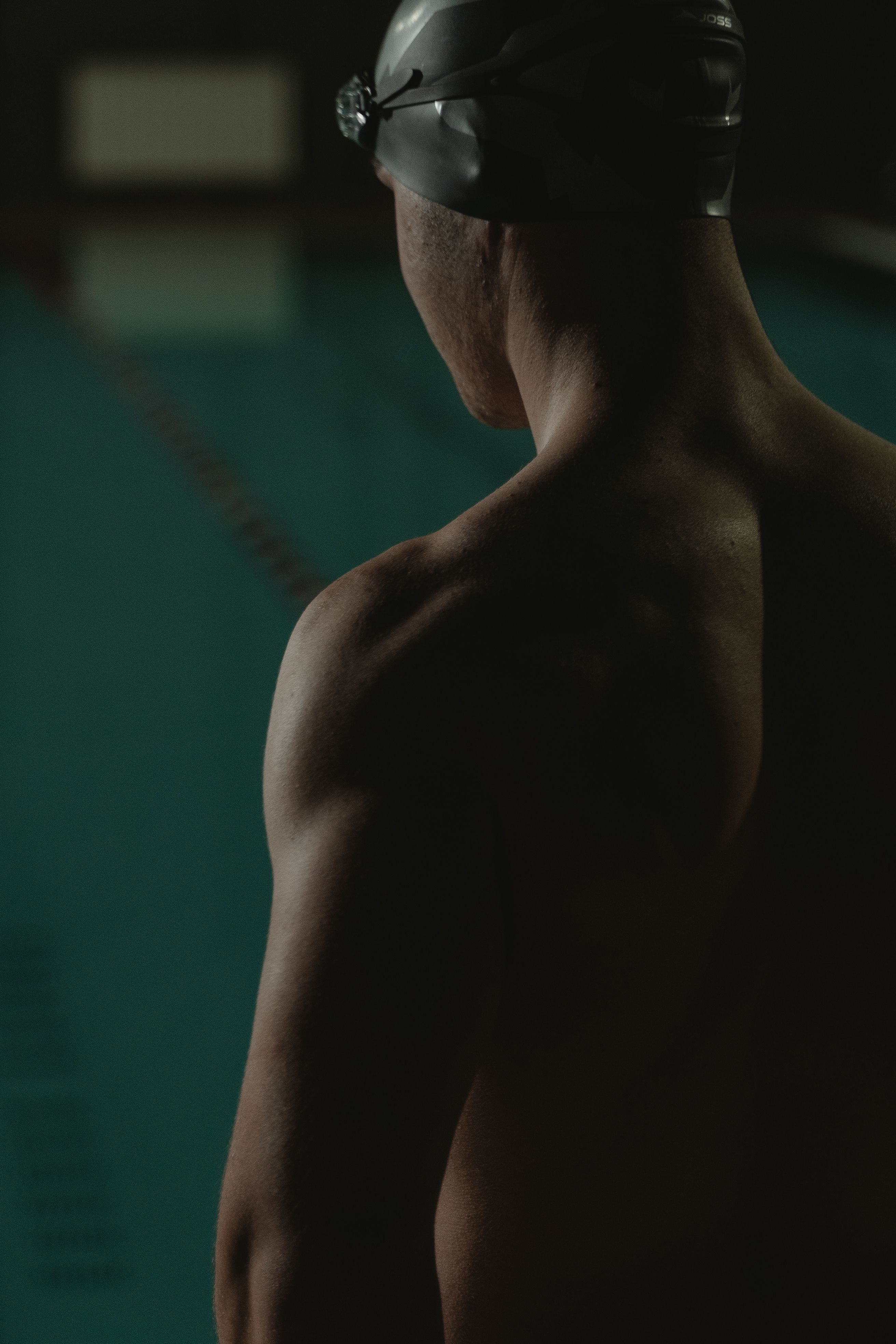 A male swimmer stands poolside, focused before a swim, illustrating athletic determination.
