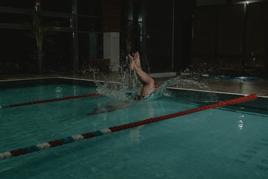 A swimmer makes a splash while diving into an indoor swimming pool during a workout.