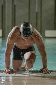 A muscular male swimmer stepping out of an indoor pool, showcasing fitness and strength.