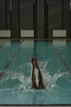 A person diving into an indoor swimming pool creating a splash, showcasing athleticism.