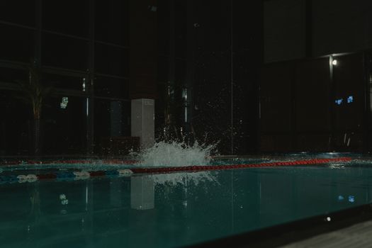 A vibrant water splash captured in an indoor swimming pool setting at night.