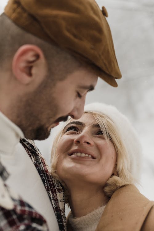 Close-Up Photo of a Man with a Beret Hat Looking at a Woman with Blond Hair