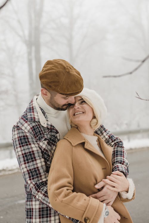 Photo of a Man with a Beret Cap Hugging a Woman in a Brown Coat