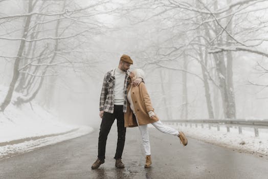 A couple sharing a tender moment on a snowy road surrounded by winter trees.