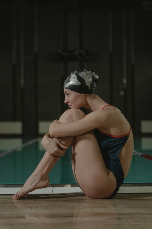 A Female Swimmer Sitting by an Indoor Swimming Pool