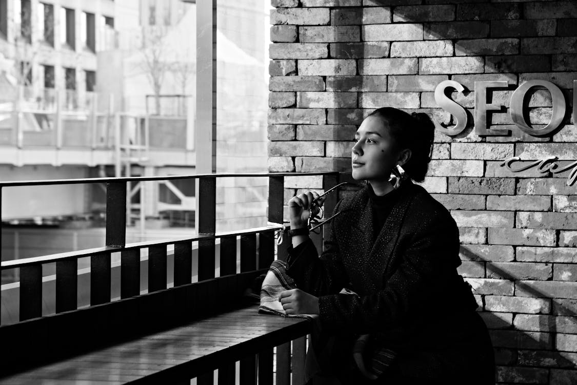 Black and white of thoughtful young female resting at table in coffee shop and looking away