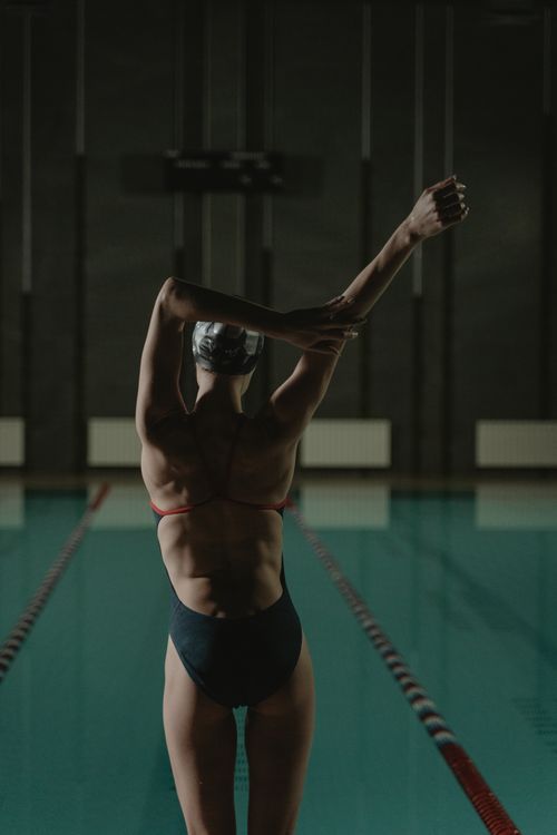 Free Back view of a woman swimmer stretching at an indoor pool, preparing for a swim session. Stock Photo