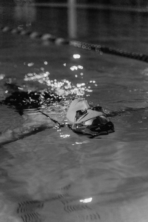 Free A swimmer with cap and goggles glides through water in a dimly lit indoor pool. Stock Photo