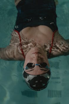 A woman in goggles and swim cap floats calmly on water, offering serene poolside vibes.