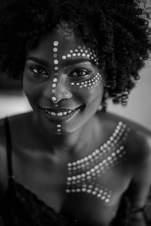 Free Black and white of cheerful African American female with paint on face and body smiling and looking at camera Stock Photo