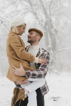 A couple shares a joyful embrace in a snowy winter forest, exuding warmth and affection.