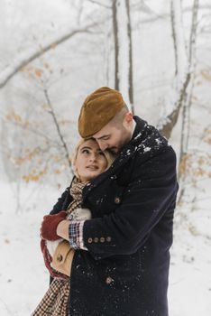 A couple embraces lovingly in a snowy forest, sharing a romantic moment.