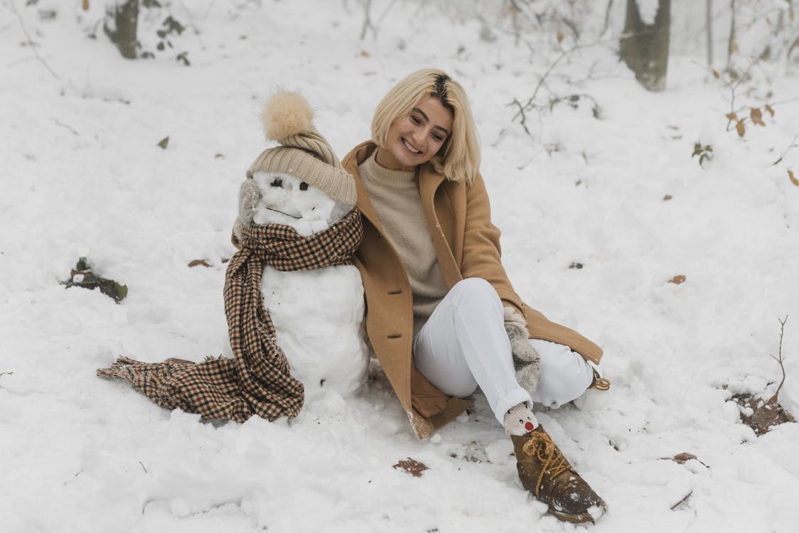 Free Happy Woman Sitting on Snow Covered Beside the Snowman Stock Photo