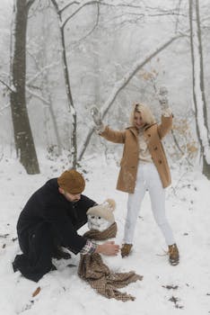 Happy couple building a snowman in a snowy forest, enjoying winter fun.