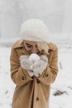 Woman in winter clothes holding snowball, expressing joy outdoors in a snowy setting.