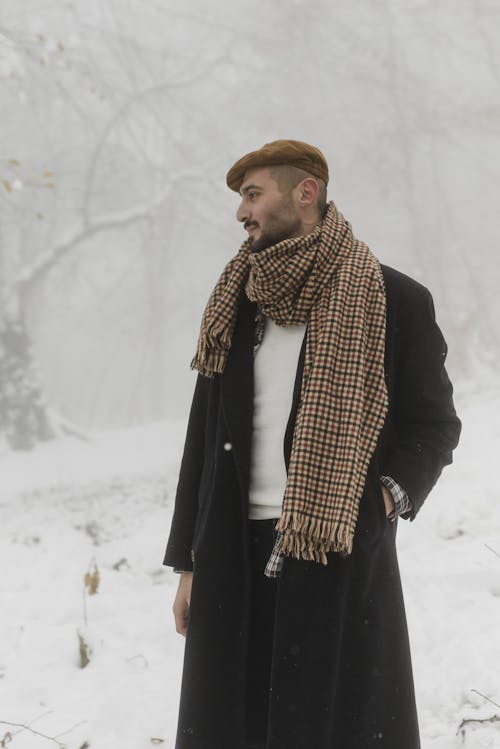 Pria Berjubah Hitam Dan Syal Coklat Putih Berdiri Di Atas Tanah Yang Tertutup Salju
