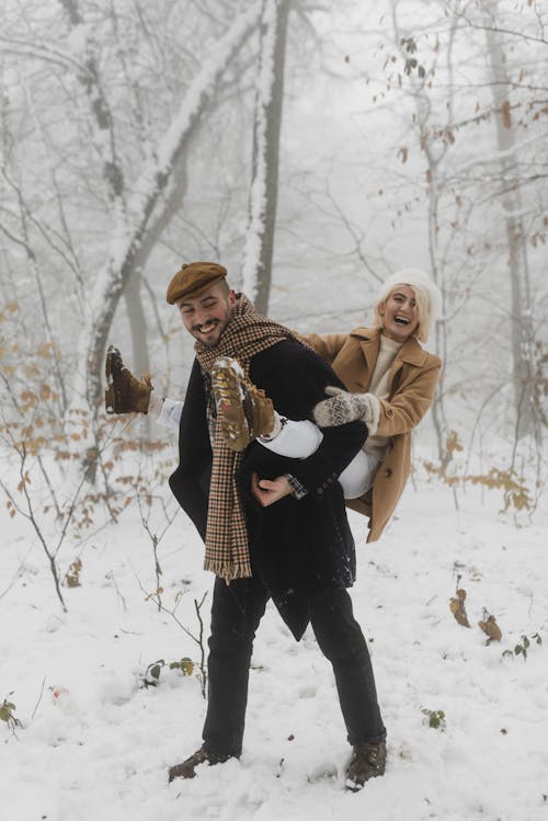Wanita Dengan Topi Rajut Coklat Menggendong Bayi Dengan Jaket Hitam Di Tanah Yang Tertutup Salju