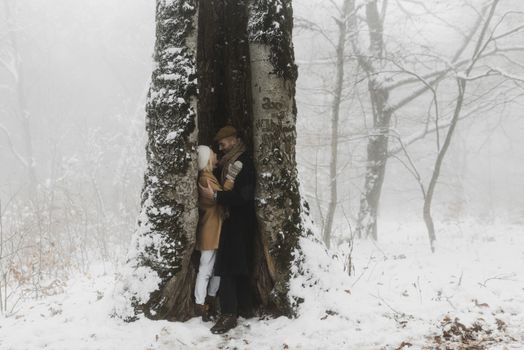 Romantic couple embracing near snowy tree, capturing warmth and love in a wintry forest setting.