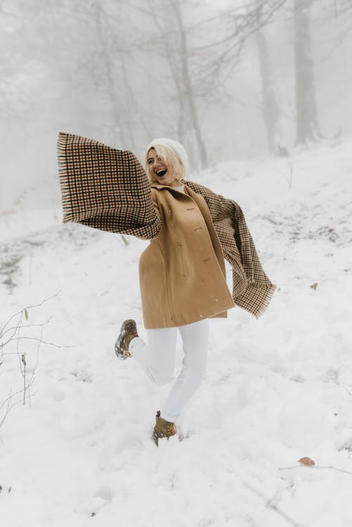 Wanita Dengan Mantel Coklat Dan Celana Putih Memegang Payung Kotak Kotak Putih Dan Hitam Berjalan Di Atas Salju
