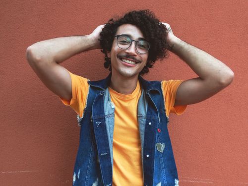 Free Portrait of a smiling man with curly afro hair and eyeglasses wearing a denim vest. Stock Photo