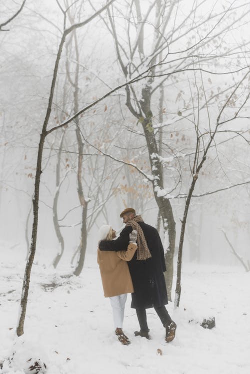 黑色外套的女人站在附近的白雪覆蓋的裸樹上