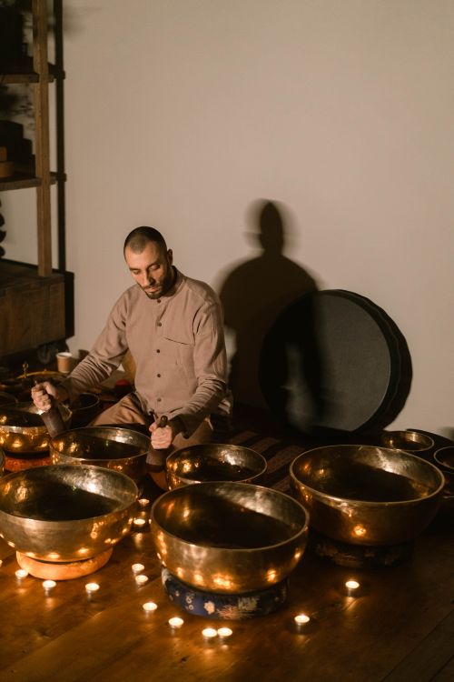 Free Man plays Tibetan singing bowls indoors, surrounded by candles for a meditative practice. Stock Photo