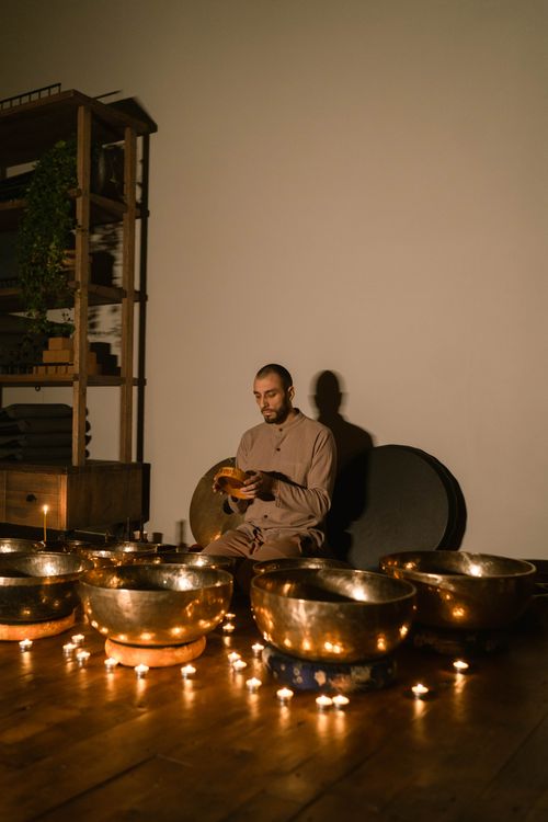 Free Man meditating with Tibetan singing bowls and candles, creating a serene atmosphere indoors. Stock Photo