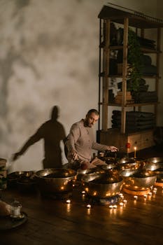 A man plays Tibetan singing bowls indoors, creating a calming atmosphere for meditation.